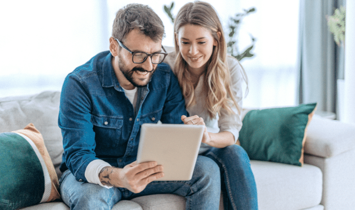 Mann und Frau sitzen auf der Couch und blicken in ein Tablet