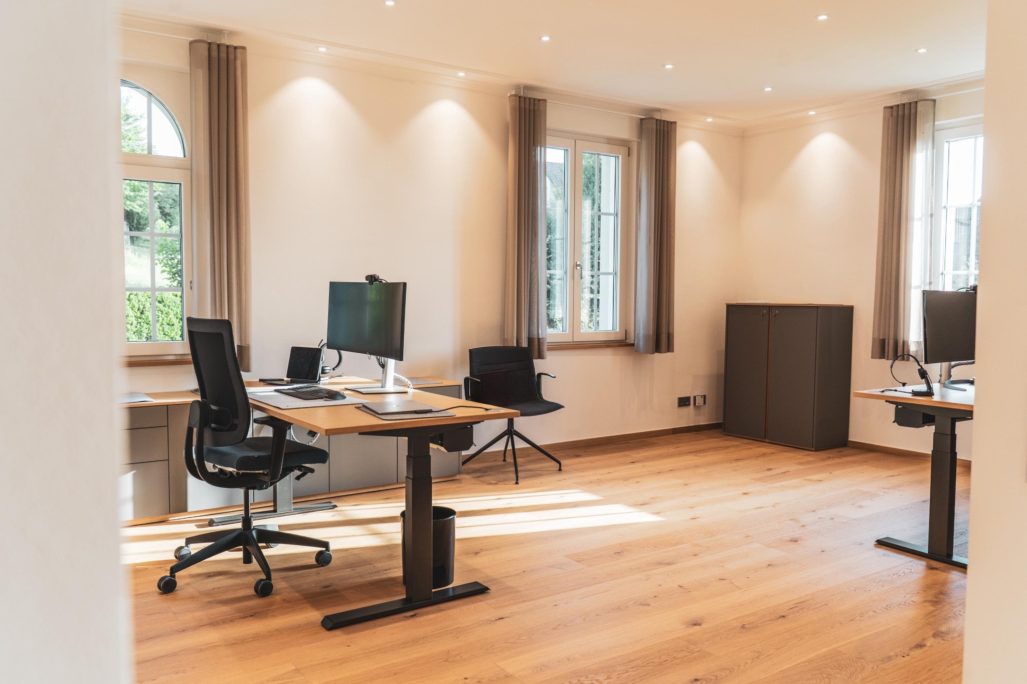 Heller, moderner Büroraum in der Ortenau mit zwei höhenverstellbaren Schreibtischen, ergonomischen Bürostühlen, großen Fenstern mit Tageslicht und Holzfußboden in ruhiger Arbeitsumgebung.